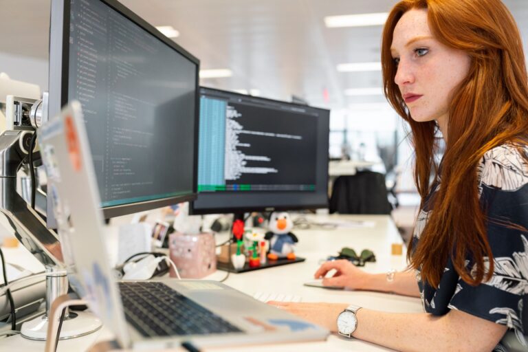Programistka pracująca przy kodzie na dwóch monitorach w biurze